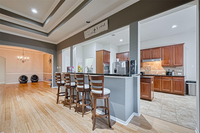 kitchen featuring a breakfast bar, ornamental molding, backsplash, dark countertops, and appliances with stainless steel finishes