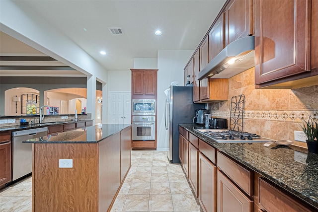kitchen featuring a sink, dark stone countertops, visible vents, range hood, and appliances with stainless steel finishes
