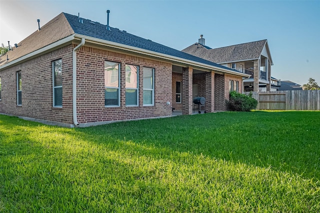 back of house featuring a yard, brick siding, a chimney, and fence