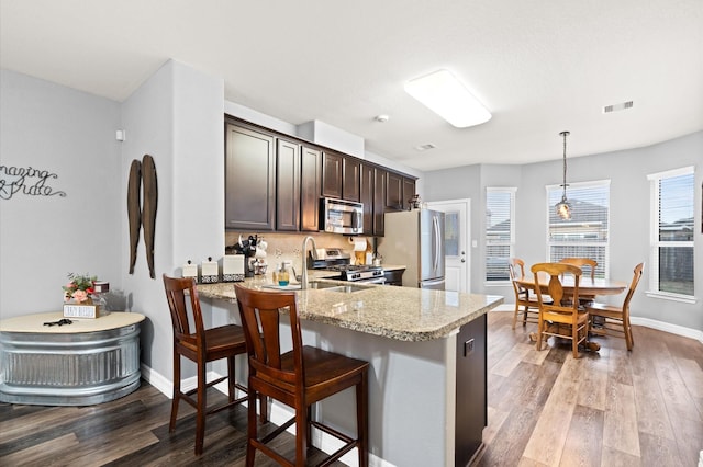kitchen featuring dark brown cabinets, light stone counters, visible vents, wood finished floors, and stainless steel appliances