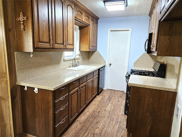 kitchen featuring a sink, wood finished floors, gas range, light countertops, and stainless steel dishwasher