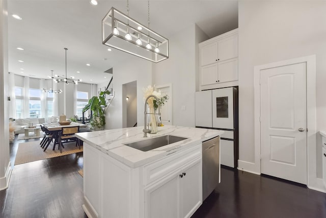 kitchen with an inviting chandelier, an island with sink, a sink, white cabinetry, and dishwasher