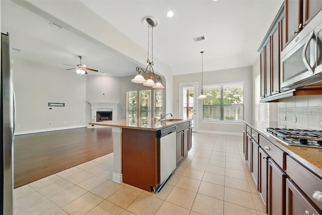 2106 Wild Peregrine Cir, Katy, TX 77494 - kitchen featuring stainless steel appliances, a fireplace with raised hearth, ceiling fan, a sink, and backsplash