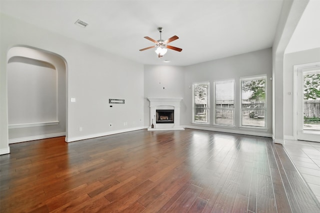 2106 Wild Peregrine Cir, Katy, TX 77494 - unfurnished living room with a ceiling fan, wood finished floors, a fireplace with raised hearth, baseboards, and arched walkways