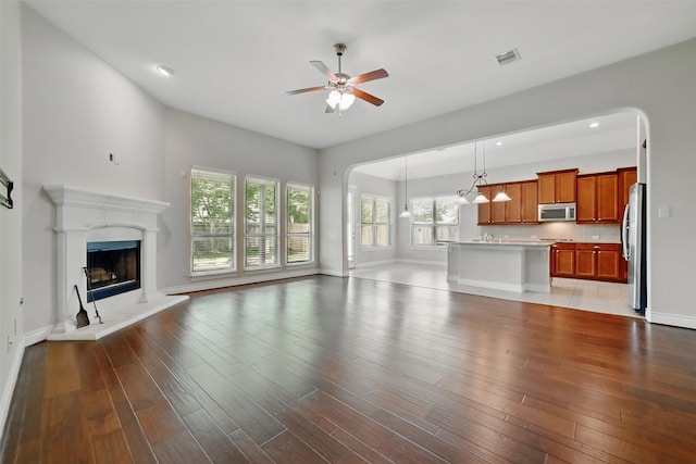 2106 Wild Peregrine Cir, Katy, TX 77494 - unfurnished living room with a ceiling fan, arched walkways, a fireplace with raised hearth, wood finished floors, and recessed lighting