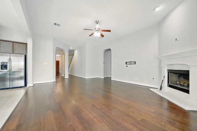 2106 Wild Peregrine Cir, Katy, TX 77494 - unfurnished living room featuring arched walkways, ceiling fan, wood finished floors, a fireplace with raised hearth, and baseboards