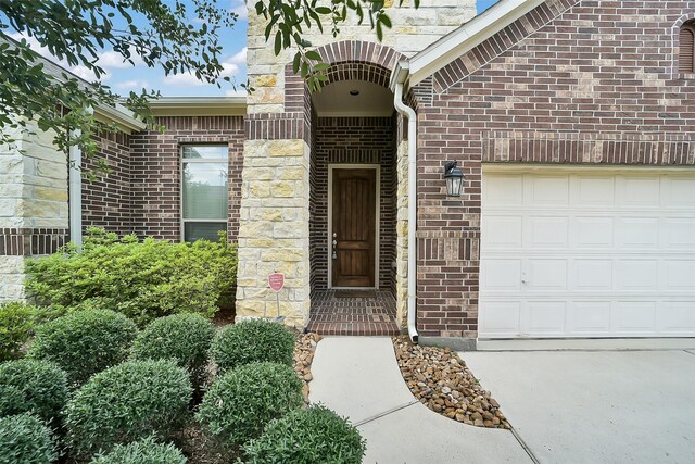 2106 Wild Peregrine Cir, Katy, TX 77494 - view of exterior entry with a garage, brick siding, concrete driveway, and stone siding