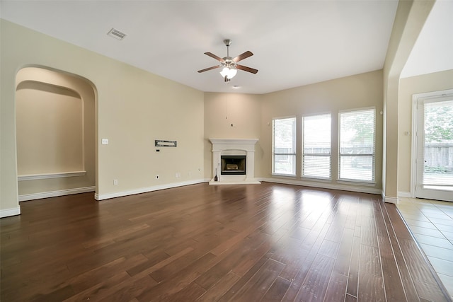 2106 Wild Peregrine Cir, Katy, TX 77494 - unfurnished living room featuring dark wood finished floors, a ceiling fan, a fireplace with raised hearth, and arched walkways