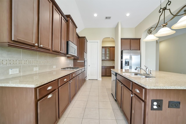 2106 Wild Peregrine Cir, Katy, TX 77494 - kitchen with stainless steel appliances, a kitchen island with sink, decorative backsplash, light tile patterned flooring, and arched walkways
