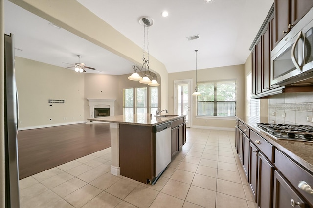2106 Wild Peregrine Cir, Katy, TX 77494 - kitchen with stainless steel appliances, dark brown cabinets, ceiling fan, light tile patterned floors, and a fireplace with raised hearth
