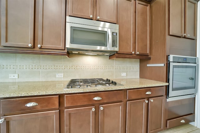 2106 Wild Peregrine Cir, Katy, TX 77494 - kitchen featuring appliances with stainless steel finishes, tasteful backsplash, light stone countertops, and brown cabinetry