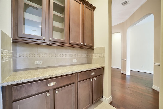2106 Wild Peregrine Cir, Katy, TX 77494 - kitchen with arched walkways, glass insert cabinets, dark wood finished floors, tasteful backsplash, and light stone counters