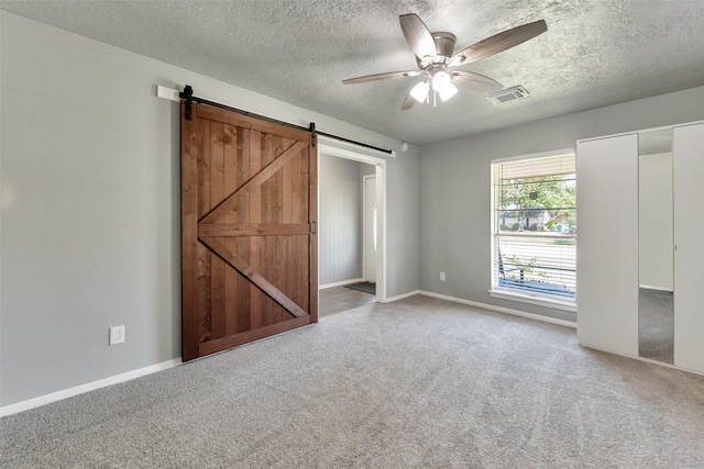 1865 El Mar Ln, Seabrook, TX 77586 - unfurnished bedroom with carpet flooring, a barn door, a textured ceiling, baseboards, and a ceiling fan