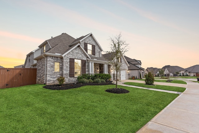traditional home with stone siding, fence, a lawn, concrete driveway, and brick siding