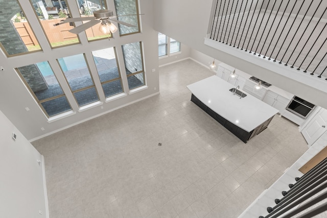 unfurnished living room with a towering ceiling, baseboards, and a ceiling fan