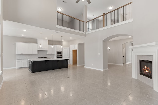 unfurnished living room with light tile patterned floors, a towering ceiling, ceiling fan, and arched walkways
