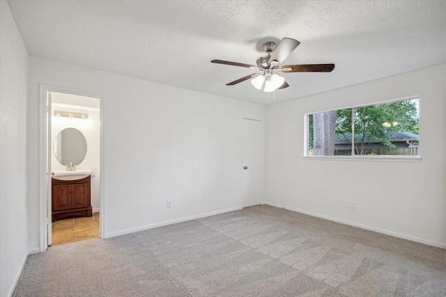 unfurnished bedroom featuring a textured ceiling, ceiling fan, carpet floors, connected bathroom, and baseboards