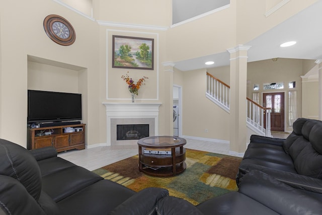 living room featuring wood finished floors, a high ceiling, ornate columns, a fireplace, and stairway