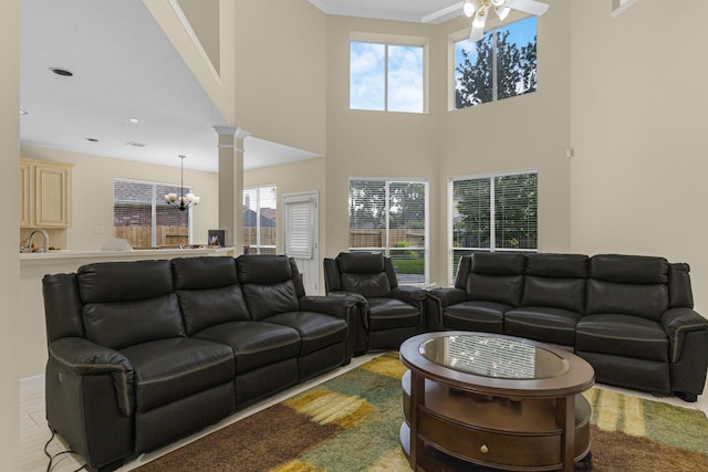 living area with plenty of natural light, decorative columns, ceiling fan with notable chandelier, and a high ceiling
