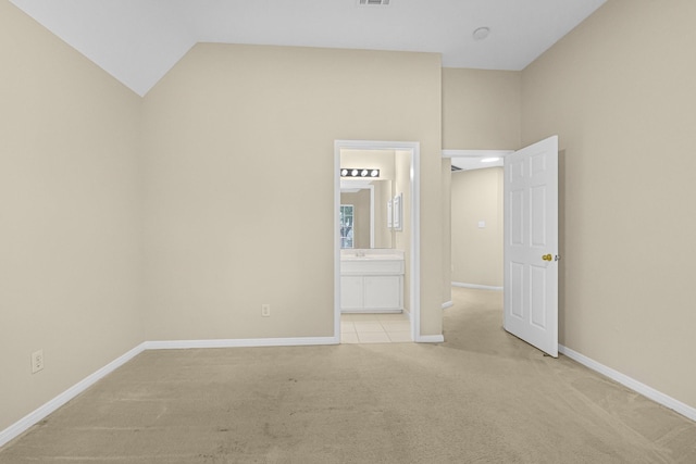 unfurnished bedroom featuring vaulted ceiling, ensuite bath, light carpet, and baseboards