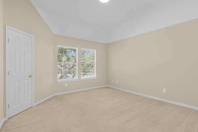 spare room featuring baseboards, lofted ceiling, and light colored carpet