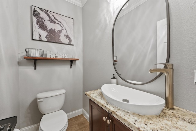 half bathroom with toilet, wood finished floors, vanity, crown molding, and baseboards