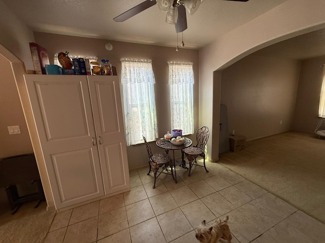 dining room with light colored carpet, light tile patterned floors, a ceiling fan, and arched walkways