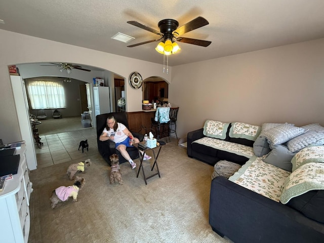 living room with carpet, a ceiling fan, visible vents, tile patterned flooring, and arched walkways