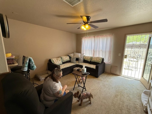 living area featuring ceiling fan, light carpet, visible vents, and a textured ceiling