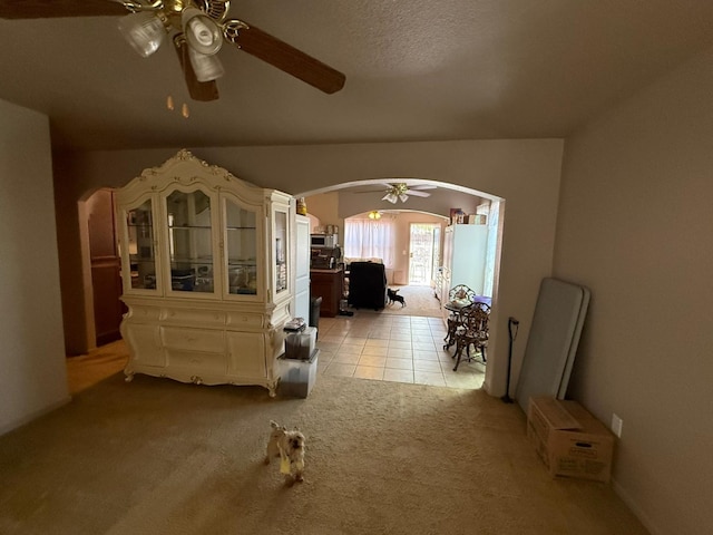 living area featuring arched walkways, light carpet, ceiling fan, and light tile patterned flooring