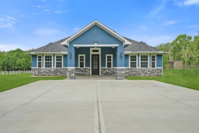 craftsman-style house featuring stone siding, stucco siding, a shingled roof, and a front lawn