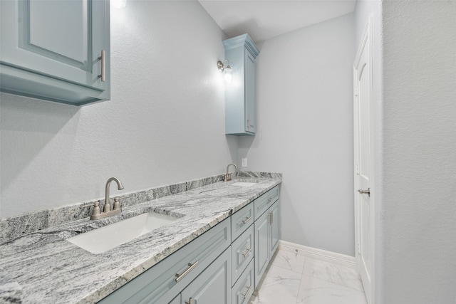full bathroom with double vanity, marble finish floor, baseboards, and a sink