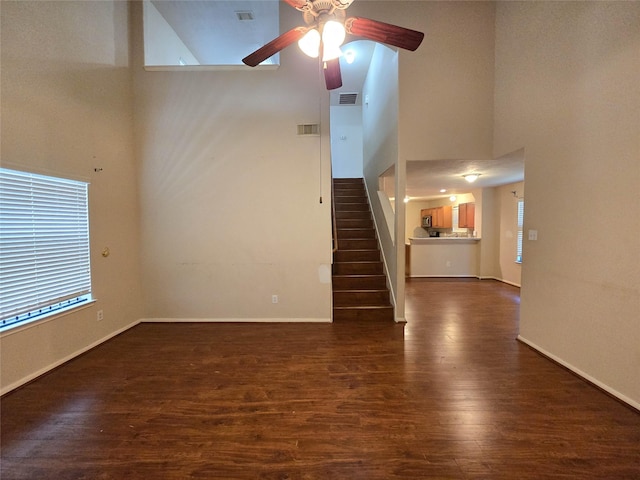 unfurnished living room with dark wood-style flooring, ceiling fan, visible vents, and a towering ceiling