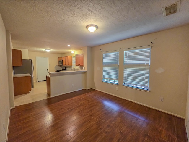 unfurnished living room with a textured ceiling, visible vents, wood finished floors, and baseboards