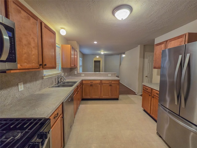 kitchen with brown cabinetry, stainless steel appliances, a peninsula, and a sink