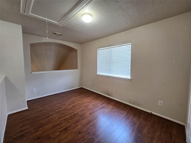 unfurnished room with attic access, a textured ceiling, baseboards, and hardwood / wood-style flooring