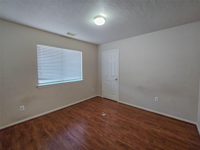 empty room featuring visible vents, wood finished floors, and baseboards