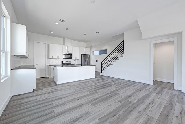 3313 Baer St, Houston, TX 77020 - kitchen featuring appliances with stainless steel finishes, white cabinetry, light wood finished floors, a kitchen island with sink, and baseboards