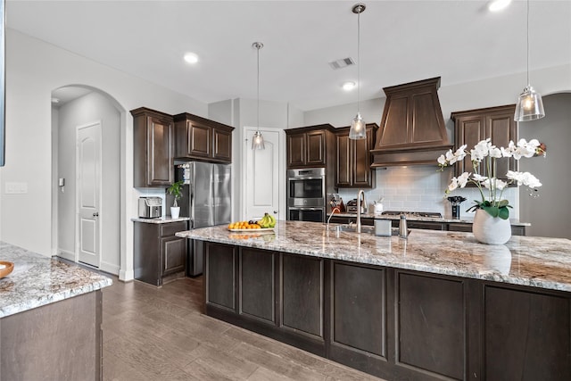 10610 Grace Hollow Dr, Cypress, TX 77433 - kitchen featuring dark brown cabinets, stainless steel appliances, visible vents, backsplash, and premium range hood