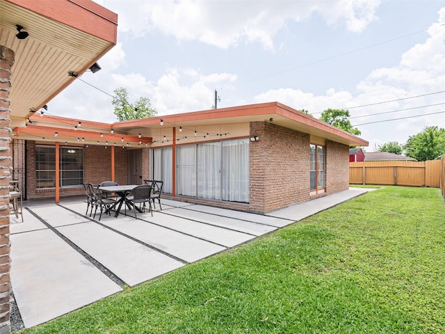 back of house featuring a yard, a patio, brick siding, and fence
