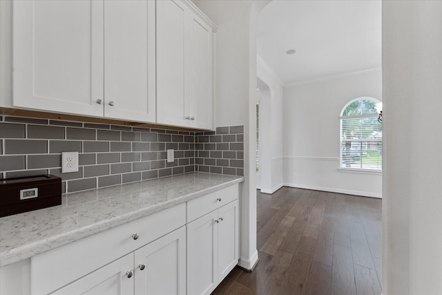 kitchen featuring white cabinets, baseboards, backsplash, crown molding, and dark wood-type flooring