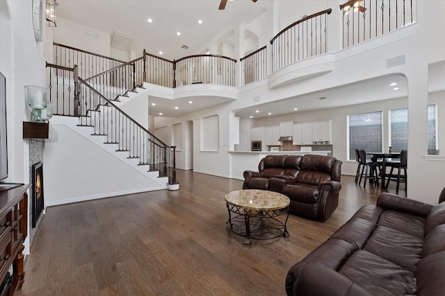 living area with a high ceiling, a stone fireplace, dark wood finished floors, stairs, and baseboards