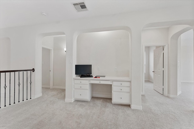 unfurnished office with light carpet, arched walkways, built in study area, and baseboards