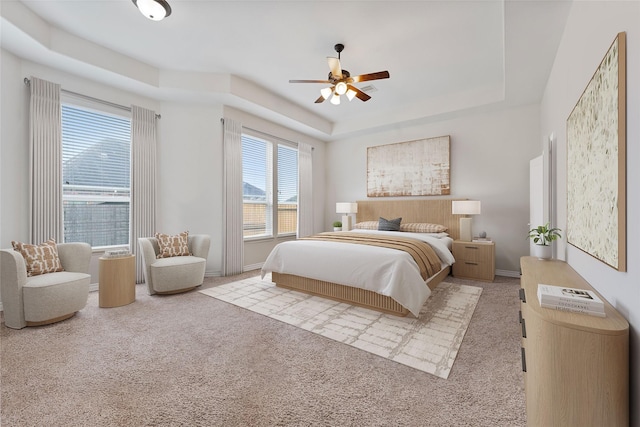 bedroom featuring carpet flooring, a tray ceiling, baseboards, and ceiling fan