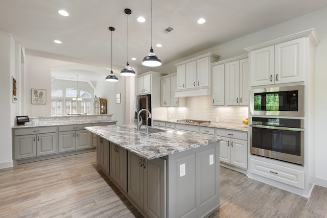 8642 Burdekin Rd, Magnolia, TX 77354 - kitchen featuring appliances with stainless steel finishes, a sink, gray cabinets, decorative backsplash, and an island with sink