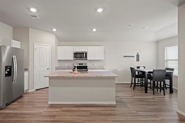 327 Pecos Dr, Huntsville, TX 77340 - kitchen with stainless steel appliances, light wood-type flooring, white cabinetry, an island with sink, and lofted ceiling