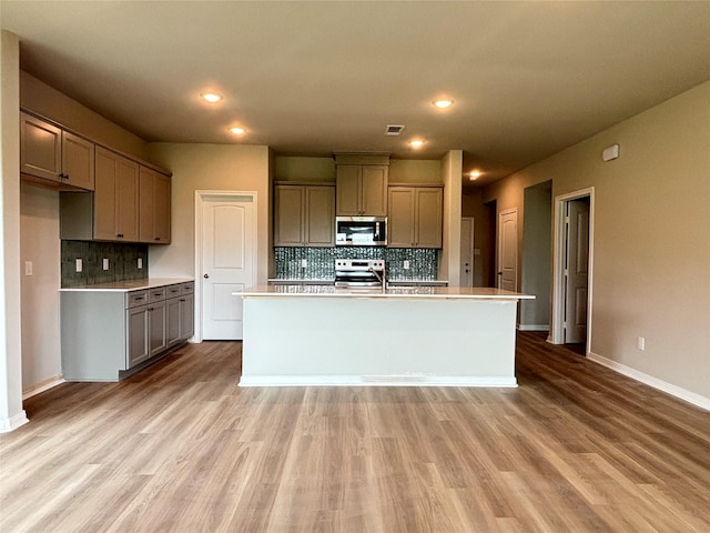 kitchen featuring backsplash, light wood finished floors, light countertops, and stainless steel appliances
