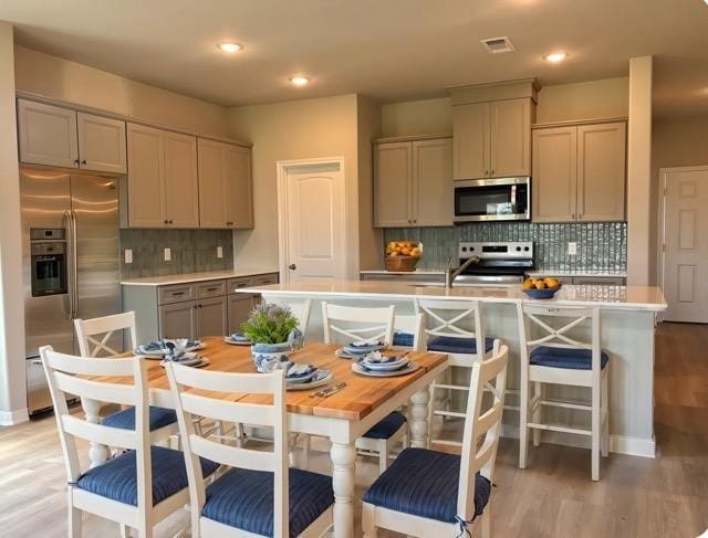 kitchen featuring tasteful backsplash, gray cabinets, light wood finished floors, light countertops, and appliances with stainless steel finishes