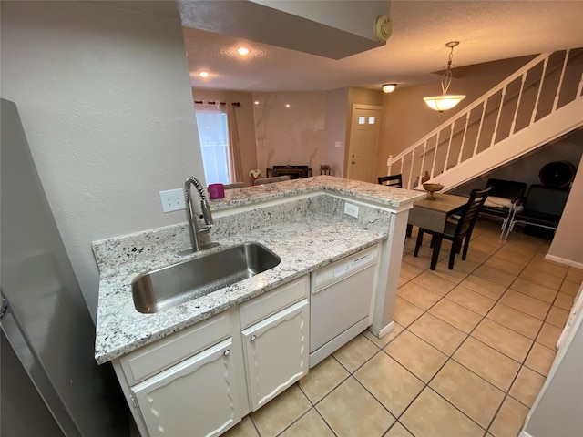 kitchen with a sink, white dishwasher, light tile patterned floors, white cabinetry, and hanging light fixtures