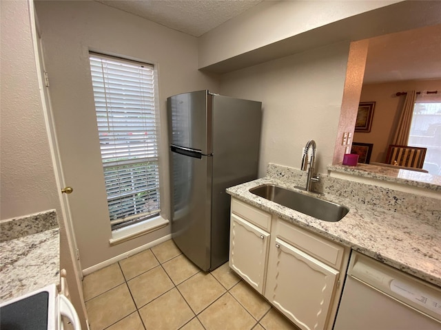 kitchen with white dishwasher, a sink, freestanding refrigerator, light tile patterned floors, and a textured ceiling